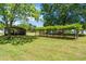 Green lawn features an open carport and vine-covered structure, set against the backdrop of a bright blue sky at 4418 Carpenter Pond Rd, Durham, NC 27703