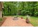 Backyard featuring brick patio with fire pit, grill, and a wooded area with play structure at 804 Warwick Ct, Burlington, NC 27215
