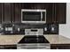 Close-up of stainless steel electric range and microwave, granite counters, and dark backsplash and cabinets at 1013 Fieldmere Pl, Wendell, NC 27591