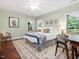 Light-filled bedroom featuring a bed, desk, chair, and windows with views of the surrounding greenery at 123 Beech Forest Way, Pittsboro, NC 27312