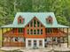 Stunning log home with green metal roof, large windows and wraparound porch surrounded by lush greenery at 123 Beech Forest Way, Pittsboro, NC 27312