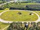 Aerial view of large equestrian course with sand surface, surrounded by grass and trees, with horse jumps and farm buildings at 128 Paraggi Ct, Clayton, NC 27527