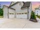 View of the two-car garage with white carriage doors and a spacious concrete driveway and landscaped garden at 46 Bonterra Way, Chapel Hill, NC 27516