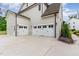 View of the two-car garage with white carriage doors and a spacious concrete driveway and landscaped garden at 46 Bonterra Way, Chapel Hill, NC 27516
