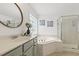 Bright bathroom featuring a round mirror, double sinks, soaking tub, glass enclosed shower, and natural light at 5213 Holly Ridge Farm Rd, Raleigh, NC 27616