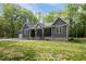 Charming gray home featuring a covered porch and landscaped front yard, nestled among lush trees at 5402 Shealtiel Way, Rougemont, NC 27572