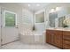 A well-lit bathroom featuring a corner soaking tub, white tile flooring, and a door to the backyard at 6509 Mountain Brook Ln, Raleigh, NC 27615