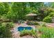 Secluded backyard pond surrounded by lush greenery, accented by a seating area with umbrella coverage at 800 Oxbow Crossing Rd, Chapel Hill, NC 27516
