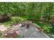 An outdoor fire pit with stone surround and chairs, surrounded by lush greenery at 800 Oxbow Crossing Rd, Chapel Hill, NC 27516