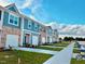 View of new townhomes featuring brick and siding exteriors, white garages, landscaping, and sidewalks under a bright, cloudy sky at 117 N Chubb Rdg, Wilson's Mills, NC 27520