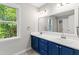Bathroom featuring double sinks, blue cabinets, large window, and a large mirror at 2 Great Oak Ct, Durham, NC 27713