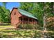 Charming log cabin home with a green metal roof and a welcoming front porch surrounded by lush greenery at 515 Tramway West Rd, Sanford, NC 27330