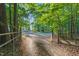 Gravel driveway leading through a gated entrance, framed by mature trees and lush greenery at 54 Malcolm Neal Path, Louisburg, NC 27549