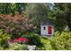 Charming backyard shed with a red door, nestled among mature trees and colorful flowers in a tranquil setting at 19 Oak Dr, Durham, NC 27707