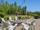 Outdoor stone firepit encircled by a brick patio and six white Adirondack chairs in a landscaped backyard at 1701 Bodwin Ln, Apex, NC 27502