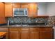 Kitchen featuring a stainless steel microwave, mosaic backsplash, wooden cabinets, and granite counters at 117 Castlerock Dr, Durham, NC 27713