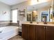 Bright bathroom featuring a soaking tub, double vanity, neutral tile, and a large mirror at 1909 Whirlaway Ct., Cary, NC 27519