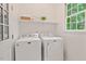 Well-lit laundry area with a window, featuring a modern washer and dryer set and overhead shelving at 4900 American Dr, Durham, NC 27705