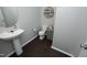 A tidy half bath with pedestal sink, toilet, decorative wall shelf, and dark wood-look floors at 621 Childsberg Way, Hillsborough, NC 27278