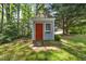 Backyard outbuilding with a red door, window box, mature trees, and a manicured lawn at 1806 Carrington Dr, Raleigh, NC 27615