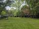 Exterior view of red house with deck and mature trees in green grassy backyard at 915 Phils Creek Rd, Chapel Hill, NC 27516