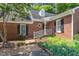 Up close of a charming one-story brick home featuring black shutters, complimented by lush landscaping and a verdant tree at 1623 Village Glenn Dr, Raleigh, NC 27612