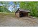 Single-vehicle carport with a brick base and corrugated metal roof, nestled in a wooded area with a gravel driveway at 4701 Brock Dr, Hurdle Mills, NC 27541