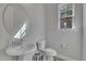 Stylish half bathroom featuring a pedestal sink, round mirror, and natural light at 112 Serenata Dr, Holly Springs, NC 27540