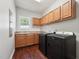Laundry room featuring a wood floor, a window, wood cabinets, a sink, and black washer and dryer at 11916 Deneb Ct, Raleigh, NC 27614
