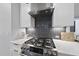 Close-up of modern gas range with a stylish backsplash, stainless steel vent hood, and white cabinets at 221 Woodsborough Pl, Raleigh, NC 27601
