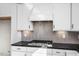 Close-up of a gas cooktop and herringbone backsplash, complemented by white cabinetry and black countertops at 436 Golden Dragonfly St, Wake Forest, NC 27587