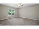 This unfurnished bedroom features neutral walls and carpet, a ceiling fan, and a large window at 5414 Stanley Rd, Durham, NC 27704