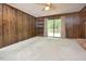 Living room with neutral carpet, wood paneled walls, ceiling fan and sliding glass doors to back deck at 5825 Scalybark Rd, Durham, NC 27712