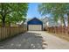 Detached blue garage with a concrete driveway and a white door is surrounded by a wooden fence and lush green trees at 420 Marsh Landing Dr, Holly Springs, NC 27540