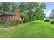 View of the backyard showcasing mature trees, a brick chimney, and well-manicured lawn at 502 Hiddenbrook Dr, Durham, NC 27703