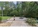 Backyard patio with a stone fire pit, landscaping, and views of the surrounding woods at 1005 Collins Dr, Raleigh, NC 27609