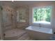 A luxurious bathroom featuring a soaking tub under a window and a glass-enclosed shower with marble surround at 1444 Old Apex Rd, Cary, NC 27513