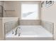 Elegant soaking tub with tiled surround and natural light from the window, providing a spa-like experience at 3832 Stovall Dr, Haw River, NC 27258