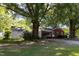 Exterior view of a brick home, a covered carport and a white storage shed surrounded by mature trees at 210 S Hughes St, Apex, NC 27502