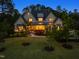 Striking two-story home surrounded by lush trees and greenery with warm lighting at dusk at 5125 Avalaire Oaks Dr, Raleigh, NC 27614