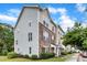 View of three-story townhomes with stone accents and a manicured lawn under a bright blue, cloudy sky at 1001 Tender Dr, Apex, NC 27502