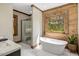 Elegant bathroom features a standalone tub and wood paneling around a window with a green view at 2092 Winwood Farm Rd, Creedmoor, NC 27522