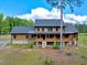 Two-story log cabin-style home featuring a raised porch and set against a backdrop of trees and blue skies at 2092 Winwood Farm Rd, Creedmoor, NC 27522