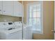 Bright laundry room features a modern washer and dryer, with upper cabinets and a window letting in natural light at 4667 Freedom Dr, Burlington, NC 27215