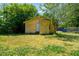 Charming one-story yellow home featuring a mature tree and yard with overgrown grass at 105 E Cole St, Dunn, NC 28334