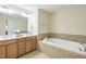 Bathroom with dual sinks, large mirror, soaking tub with tile surround, and ample counter space at 221 Mayfield Dr, Apex, NC 27539