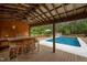 Inviting covered outdoor living space with bar area overlooks a pristine pool and wooded backyard at 3653 Range Rd, Stem, NC 27581