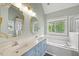 Bathroom with blue cabinets, double sinks, mirrors, and a soaking tub with a window at 640 St Vincent Dr, Holly Springs, NC 27540
