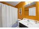Well-lit bathroom featuring orange walls, white fixtures, a shower with a curtain, and decorative art at 1303 Bent Willow Dr, Durham, NC 27704