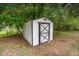 Small white and black shed in a wooded backyard with a secure door and adjacent trees at 2670 Nc 210 S, Lillington, NC 27546
